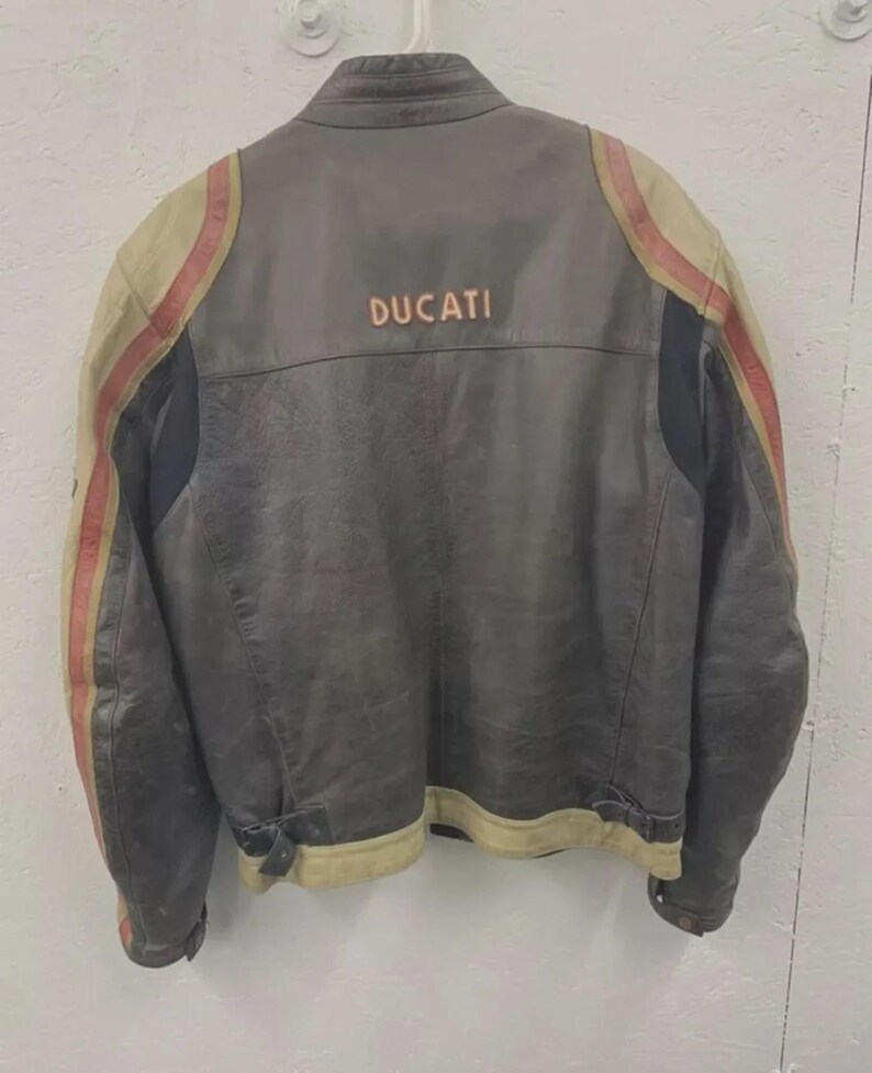 May include: A vintage gray leather motorcycle jacket with the word "DUCATI" across the back. The jacket features tan and red stripes on the sleeves and tan trim along the bottom.