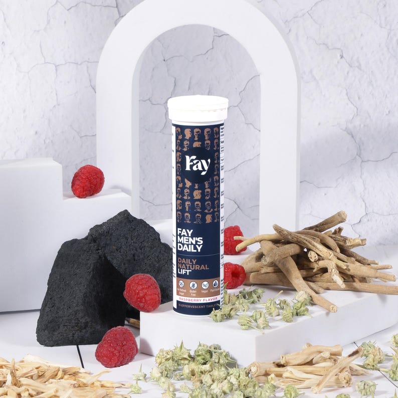May include: A white and blue tube of "Fay Men's Daily Natural Lift" effervescent tablets, with a raspberry flavor. The tube is surrounded by fresh raspberries, wood pieces, and green herbs. The background is white.
