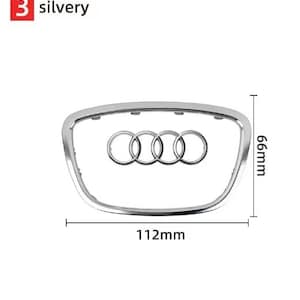 May include: A silvery car emblem with the number 3 in a red square. The emblem is a silver frame with the Audi logo in the center. The dimensions are 11.2cm wide and 6.6cm high.