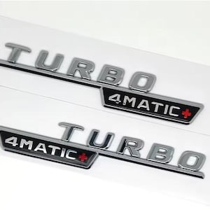 May include: Two chrome-colored "TURBO 4MATIC+" emblems. The word "TURBO" is in a bold, sans-serif font, and "4MATIC+" is in a black rectangle with a red plus sign. The emblems are on a white background.
