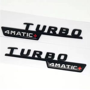 May include: Two black "TURBO" emblems with "4MATIC+" in white text. The "4MATIC+" emblem has a red plus sign. The emblems are on a white background.