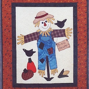 May include: A quilted wall hanging featuring a whimsical scarecrow design. The scarecrow has a straw hat, plaid arms, and blue overalls. A sign reads "Birds Beware!" Black birds and pumpkins complete the autumn-themed artwork.