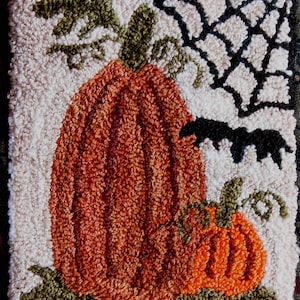 May include: Hand-tufted Halloween-themed rug featuring two orange pumpkins with green vines and leaves. A black spider web and bats are in the background. The rug has a cream-colored background and a black and orange checkered border.