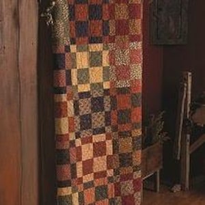 May include: A patchwork quilt with a checkerboard pattern in shades of red, brown, green, and yellow. The quilt is hanging vertically against a wooden surface, showcasing its intricate design and rustic charm. The quilt's dimensions are not visible.