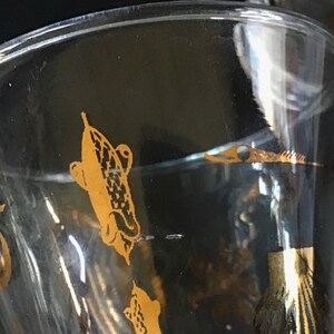 May include: A clear glass goblet with a gold design of fish. The fish are stylized and have a detailed pattern.