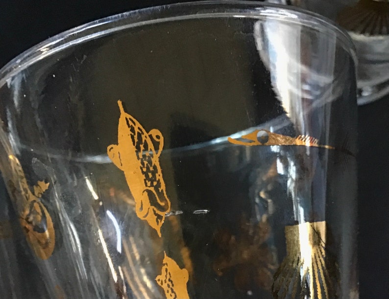 May include: A clear glass goblet with a gold design of fish. The fish are stylized and have a detailed pattern.