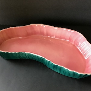 May include: A pink and green ceramic serving dish shaped like a leaf. The dish has a scalloped edge and a smooth, glossy finish.