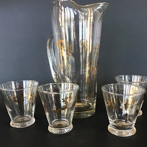 May include: A set of five clear glass drinkware pieces with gold accents. The set includes a pitcher and four glasses.