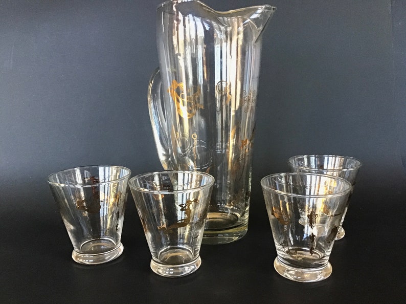May include: A set of five clear glass drinkware pieces with gold accents. The set includes a pitcher and four glasses.