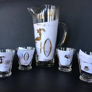 May include: A vintage glass pitcher and four matching glasses with gold and black nautical designs. The pitcher has a handle and a wide mouth. The glasses are short and have a wide base.