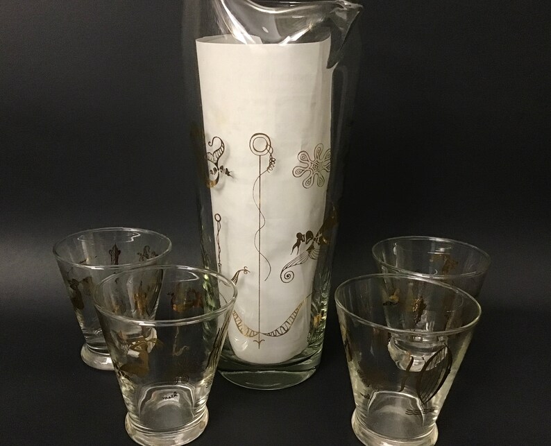 May include: A set of five vintage glass cocktail glasses with gold accents. The glasses feature a stylized design of a bird, a flower, and a spiral. The pitcher is tall and cylindrical with a wide base.