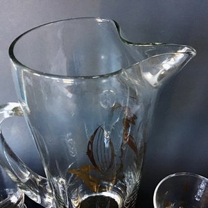 May include: A clear glass pitcher with a gold floral design. The pitcher has a handle and a wide mouth.