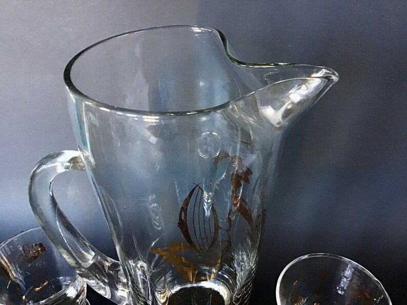 May include: A clear glass pitcher with a gold floral design. The pitcher has a handle and a wide mouth.