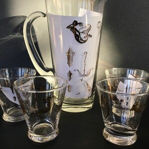 May include: A set of five clear glass drinking glasses with gold nautical designs, including a mermaid, anchor, and fish. The glasses are part of a pitcher set.