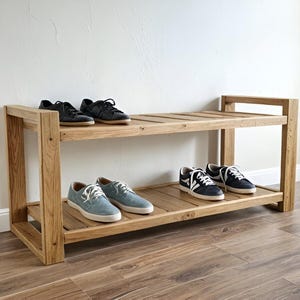 Peut inclure: Un présentoir à chaussures en bois à deux niveaux avec plusieurs paires de chaussures. Le présentoir est en bois de couleur claire et a un design rectangulaire simple. Les chaussures sont de couleurs variées, dont le noir et le bleu.
