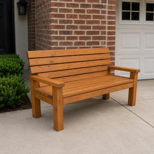 Puede incluir: Un banco de madera de color marrón medio con respaldo y asiento de listones. El banco está construido con cuatro patas cuadradas resistentes y dos reposabrazos planos, mostrando un acabado de veta de madera natural en toda la estructura.