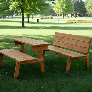 May include: A wooden picnic table with attached benches, set on a grassy lawn. The table and benches are constructed from light-colored wood, featuring a natural finish. The scene is outdoors, with trees and a park in the background.