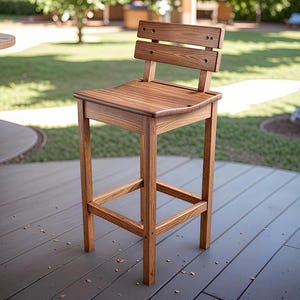 Op de afbeelding: Een lichtbruine houten barkruk. De kruk heeft een rechthoekige zitting, een rugleuning met twee horizontale latten en een voetensteun. De poten zijn recht en stevig. De kruk staat op een grijs terras, wat duidt op gebruik buitenshuis.