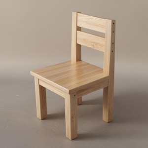 Op de afbeelding: Een kleine, lichtgekleurde houten stoel met een rechthoekige zitting en een rugleuning met twee horizontale spijlen. De stoel heeft vier stevige poten en is ontworpen voor kinderen. De houtnerf is zichtbaar.