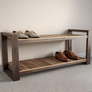 Può includere: Un porta scarpe in legno a due livelli con due paia di scarpe. Il ripiano superiore contiene scarpe stringate di colore chiaro, mentre il ripiano inferiore mostra scarpe in pelle marrone. Il porta scarpe è in legno scuro.