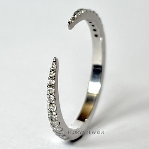 Op de afbeelding: Een zilverkleurige open ring met kleine, heldere edelstenen langs de buitenste curve. De ring heeft een modern, minimalistisch ontwerp. De merknaam "FLORYN JEWELS" is zichtbaar.