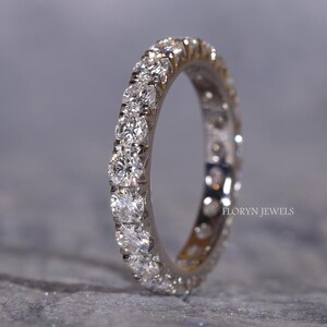 May include: A silver eternity ring with a continuous row of round, clear gemstones. The ring is set against a gray background, with the brand name "FLORYN JEWELS" visible on the ring.