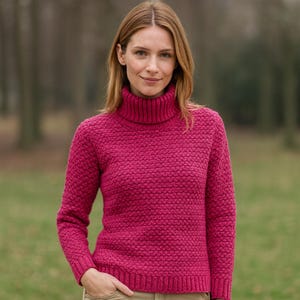 Puede incluir: Un suéter de cuello alto magenta con un patrón de punto texturizado. El suéter de manga larga tiene un dobladillo y puños acanalados. La modelo lleva el suéter al aire libre en un entorno natural.