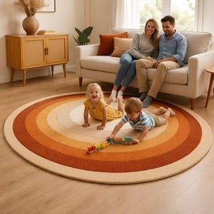 Può includere: Un tappeto rotondo con un design arcobaleno retrò nei toni dell'arancione, beige e crema. Il tappeto è su un pavimento in legno. Una famiglia è seduta su un divano sullo sfondo, con due bambini che giocano sul tappeto.