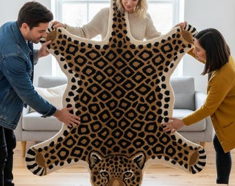 May include: A large, beige and brown leopard-print rug with a detailed leopard face at the bottom. The rug has a cream-colored border and is being held up by three people in a well-lit room.