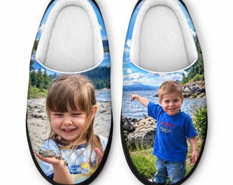 May include: A pair of custom photo slippers featuring a white plush interior lining and black trim. The left slipper displays a young girl holding a rock, while the right slipper shows a young boy in a blue shirt pointing toward a lake.