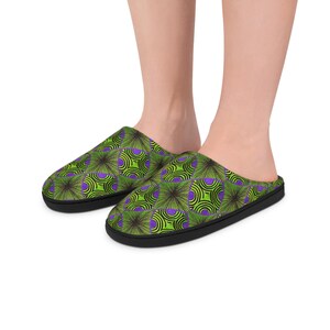 Peut inclure: Une paire de pantoufles à motifs avec une semelle noire. Les pantoufles présentent un motif répétitif de formes géométriques vertes, violettes et noires. Ces pantoufles sont conçues pour un usage intérieur.
