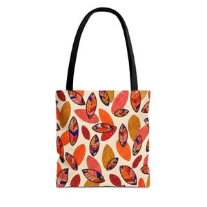 May include: A tote bag featuring a cream-colored background with a repeating pattern of stylized leaves in shades of orange, red, and brown. The leaves have dark outlines and internal geometric details. The bag has two solid black fabric shoulder straps.