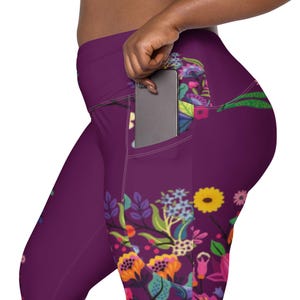 May include: Plum-colored leggings with a floral design featuring yellow, orange, and blue flowers. The leggings have a pocket on the side, with a phone partially visible inside.
