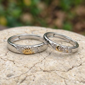 May include: Two silver adjustable rings, one with a gold sun design and the other with a gold crescent moon. The rings are set against a neutral background, showcasing their celestial theme. The rings are likely made of sterling silver.