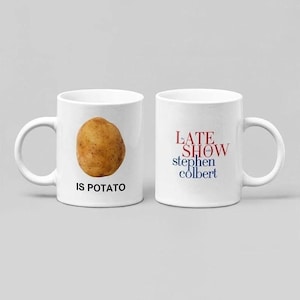 May include: Two white ceramic mugs. One mug features a brown potato with the text "IS POTATO" below it. The other mug has the words "LATE SHOW stephen colbert" in red, blue, and white.