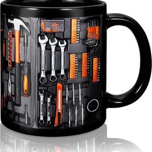 May include: Black ceramic mug featuring a toolbox design with various tools. The design includes a hammer, wrenches, screwdrivers, and other hardware in orange and silver against a black background. The mug has a curved handle.