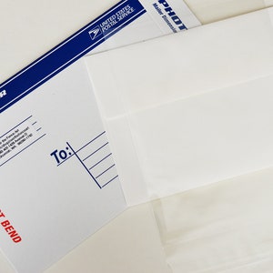 Op de afbeelding: Een witte envelop met een blauwe rand en de tekst "PHOTO MAILER" en "NIET BUIGEN". De envelop is geadresseerd aan iemand met de tekst "Van:" en "Aan:" gedrukt op de voorkant.