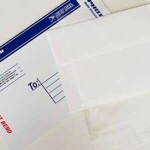 May include: A white envelope with a blue and white border. The envelope is labeled "Photo Mailer" and has the text "Do Not Bend" printed in red. The envelope is addressed to someone and has a space for the sender's address.