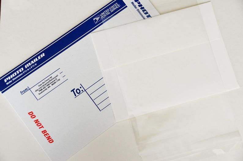 May include: A white envelope with a blue and white border. The envelope is labeled "Photo Mailer" and has the text "Do Not Bend" printed in red. The envelope is addressed to someone and has a space for the sender's address.