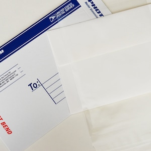 May include: A white envelope with a blue border and the text "PHOTO MAILER" and "DO NOT BEND". The envelope is addressed to someone with the text "To:" and lines for writing an address.