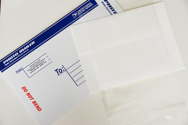 May include: A white envelope with a blue border and the text "PHOTO MAILER" and "DO NOT BEND". The envelope is addressed to someone with the text "To:" and lines for writing an address.