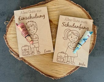 May include: Two wooden cards with engraved illustrations and text. One card features a boy holding a rolled-up item, the text reads "Alles Gute zur Einschulung" and the name "Luca". The other card shows a girl with a rolled-up item, text reads "Alles Gute zum Schulanfang" and the name "Mika".