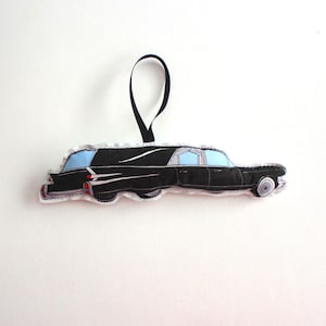 Puede incluir: Adorno de tela negro y blanco de una carroza fúnebre vintage con una ventana azul. El adorno tiene un lazo de cinta negro para colgar.