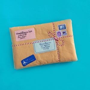 May include: A brown paper package with red and white twine tied around it. The package has several labels with text, including "Chocolaterie de Jusje", "31 Rue de Paris, France", "338131", "Madane Deonciers", "358 station", "Paris France", "973451", and "PAR AVION BY AIR MAIL".