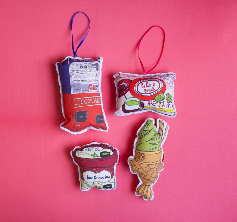 May include: Four colorful felt ornaments with Japanese-inspired designs. The ornaments feature a vending machine, a green tea ice cream cone, a green tea snack pack, and a Japanese-style fish cake.