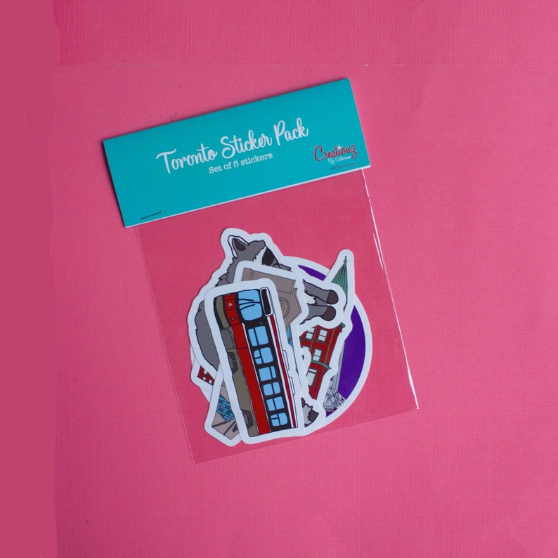 May include: A sticker pack featuring Toronto landmarks, including a streetcar, a building, and a wolf. The pack includes 5 stickers and is labeled "Toronto Sticker Pack, Set of 5 stickers, Creations by Chelsea".