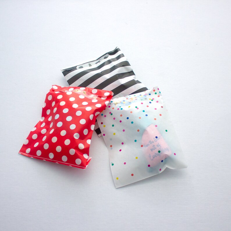 May include: Three gift bags with different patterns. One bag is red with white polka dots, one is black and white striped, and one is white with colorful confetti and the text "Have the best out of everything".