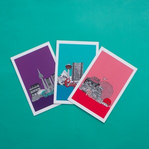 May include: Three postcards with illustrations of city skylines. The postcards are purple, blue, and pink. The text on the postcards reads "Toronto", "Calgary", and "Montreal".