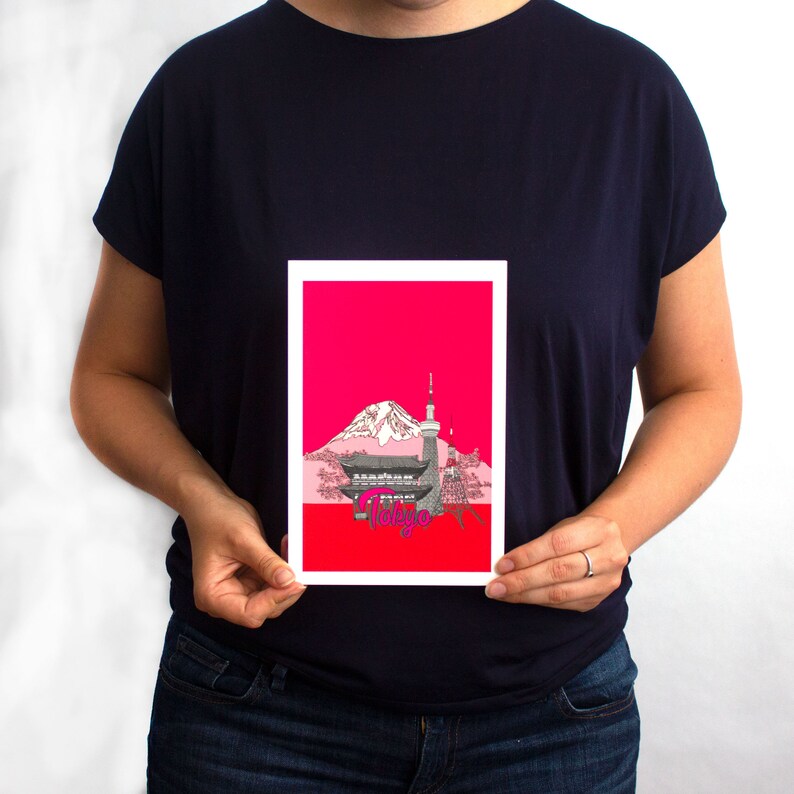 May include: A white card with a red background featuring a black and white illustration of Mount Fuji, a traditional Japanese building, and a tower. The text "Tokyo" is written in pink letters.