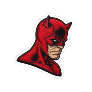 May include: Embroidered patch featuring a red superhero with a black mask and horns. The patch depicts a stern-faced character with detailed facial features and a white border. The design is a comic book style.